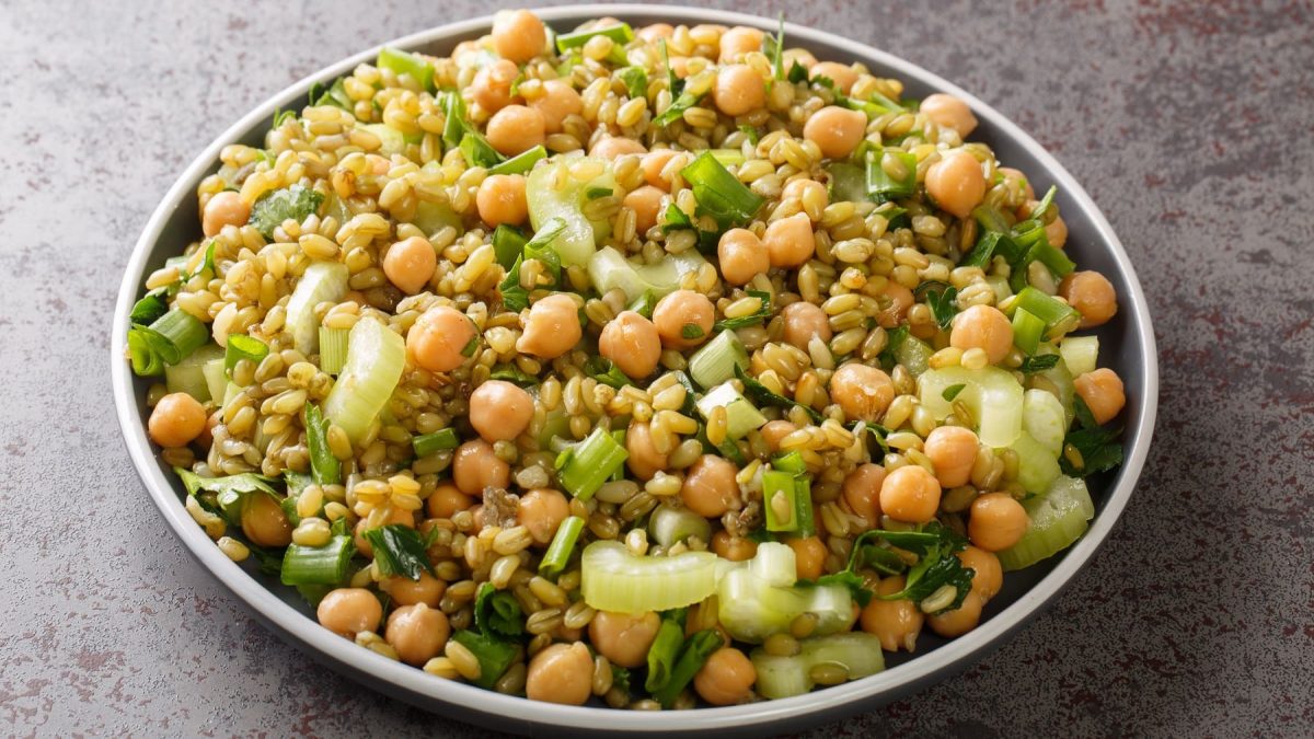 Ein grauer Teller mit dem Freekeh-Salat auf grauem Untergrund. Alles von schräg oben fotografiert.