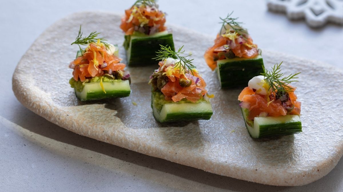 5 kleine Fingerfood-Snacks mit Avocado und Räucherlachs auf einem weißen Teller von schräg oben fotografiert.