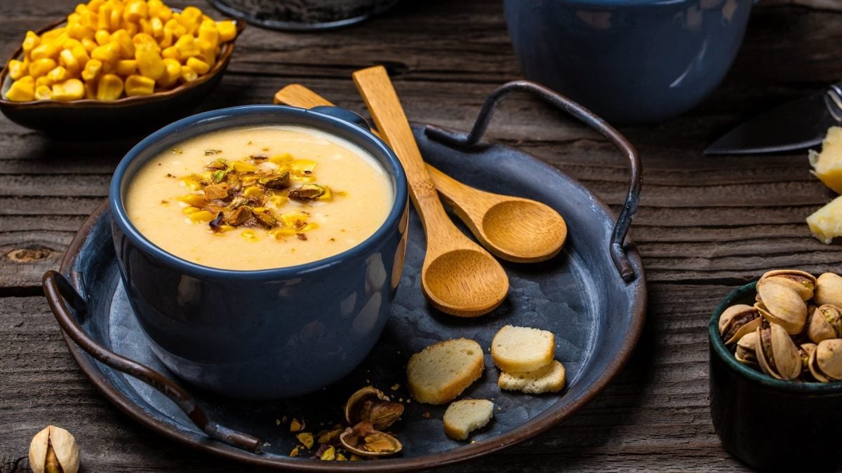 Die Maissuppe in dunkelblauem Geschirr auf einem rustikalen Holztisch. Alles von schräg oben fotografiert.