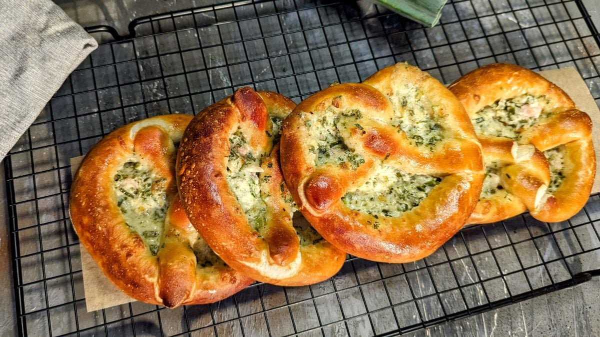 Mehrere Flammkuchen-Brezeln auf einem schwarzen Gitter und grauem Untergrund. Alles direkt von oben fotografiert.