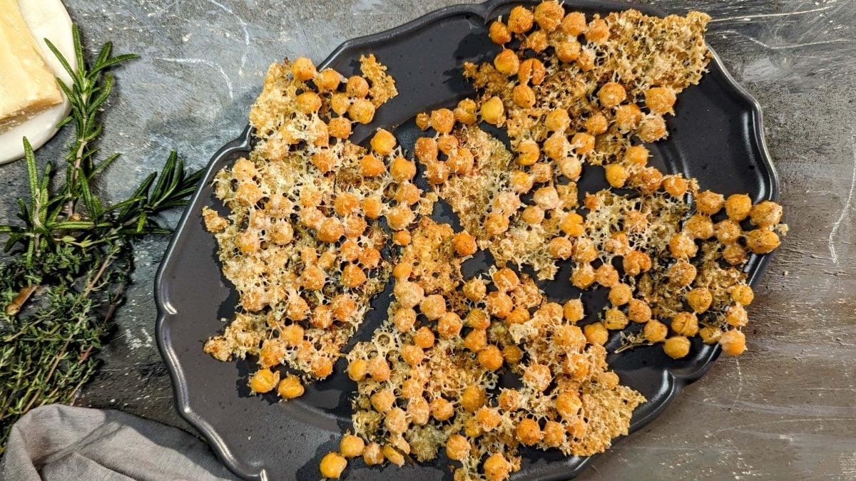Die Chips auf einem dunklen Teller und grauem Untergrund von oben fotografiert. Daneben frische Kräuter und ein Stück Parmesan.