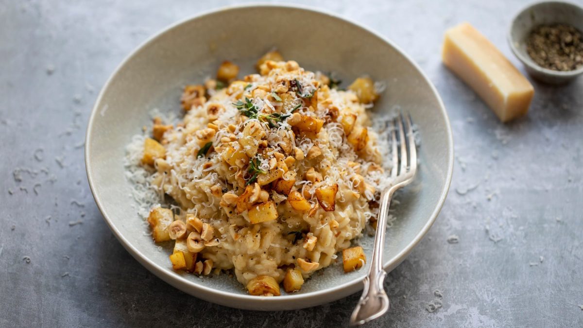 Eine graue Schale mit dem Sellerie-Risotto auf grauem Untergrund von schräg oben fotografiert.