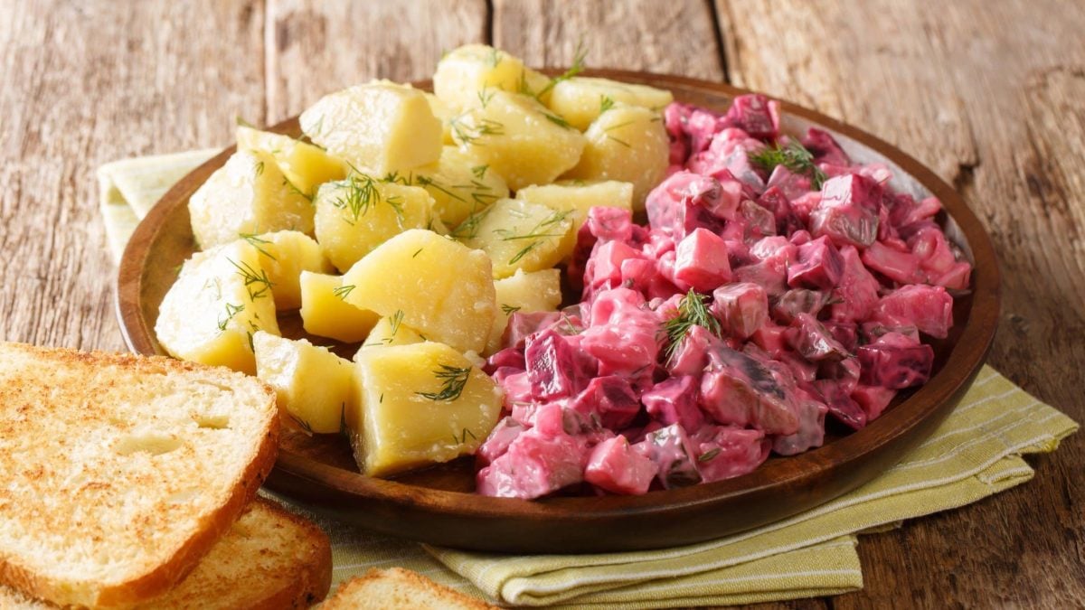Draufsicht schräg: Ein Teller Roter Heringssalat mit Kartoffeln und gerösteten Weißbotscheiben.