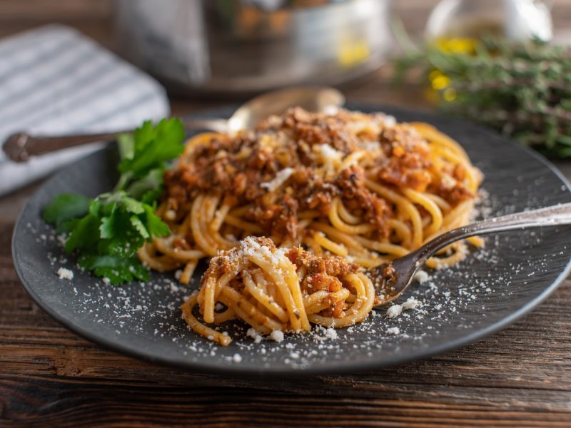 Spaghetti Bolognese bestreut mit Parmesan auf dunklem Teller und dunklem Holztisch.