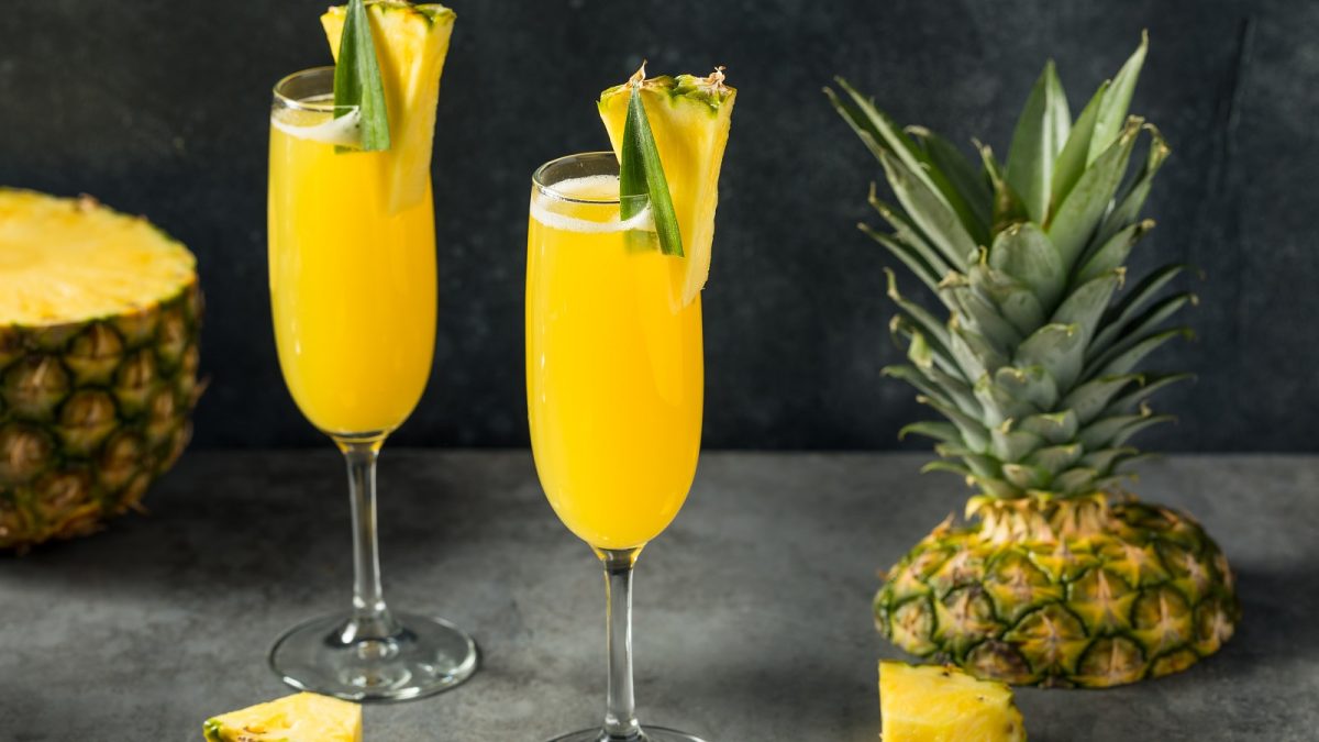Zwei Gläser Ananas-Mimosa neben frischer Ananas.