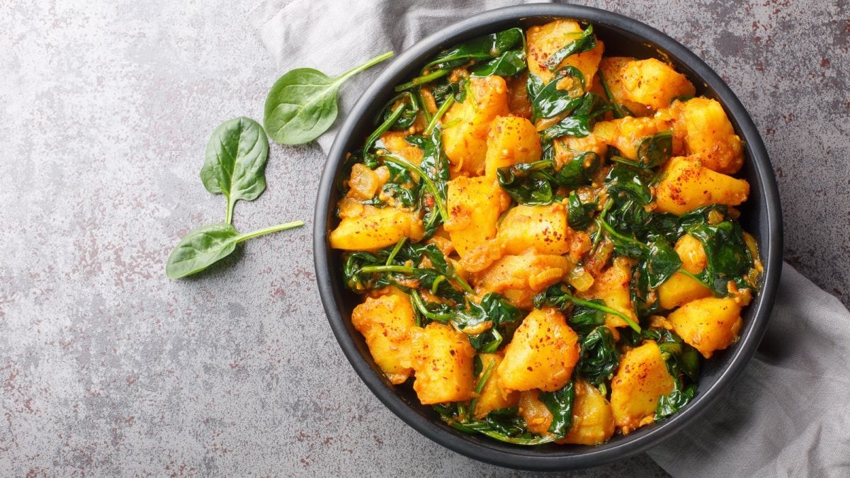 Ein schwarzer Topf mit Saag Aloo auf einem grauen Tisch.