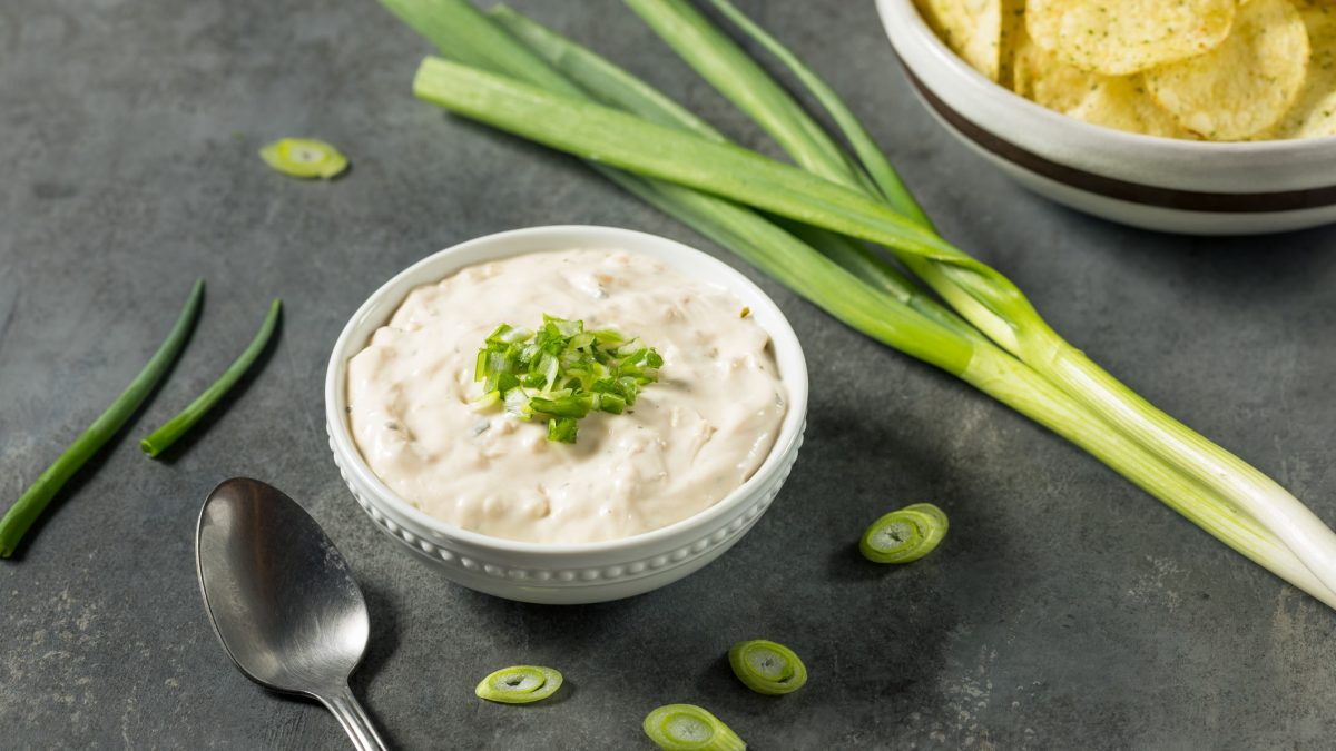 Ein weißes Schälchen mit dem Sour Cream-Dip auf grauem Untergrund.