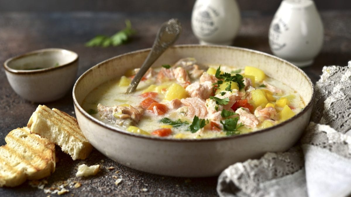 Draufsicht schräg: Eine Teller amerikanische Chowder mit Lachs steht auf einem Holztisch. Dahinter stehen ein Salz- und ein Pfefferstreuer.