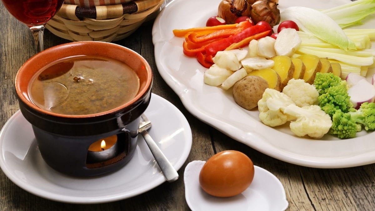 Bagna cauda in einem Stövchen. Daneben ein Ei und frisches Gemüse.
