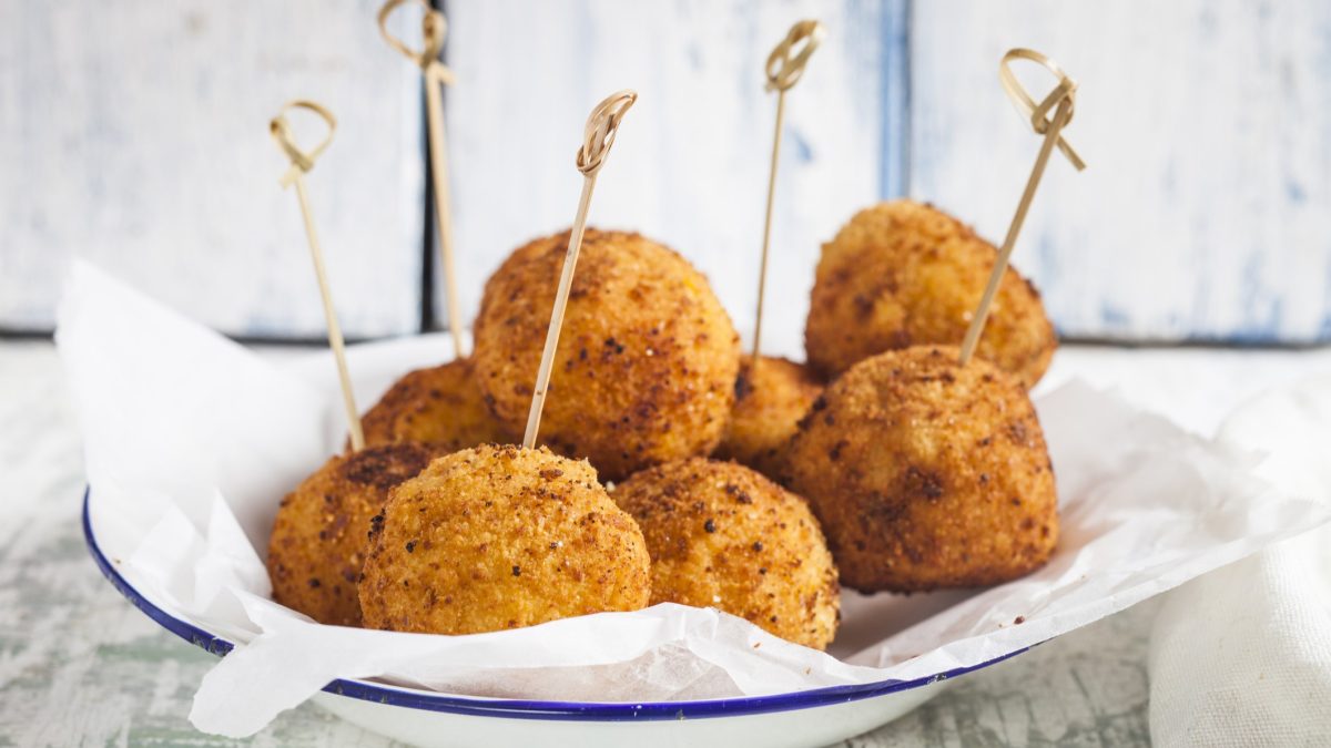Bitterballen auf einem weißen Teller mit blauem Rand von der Seite fotografiert.