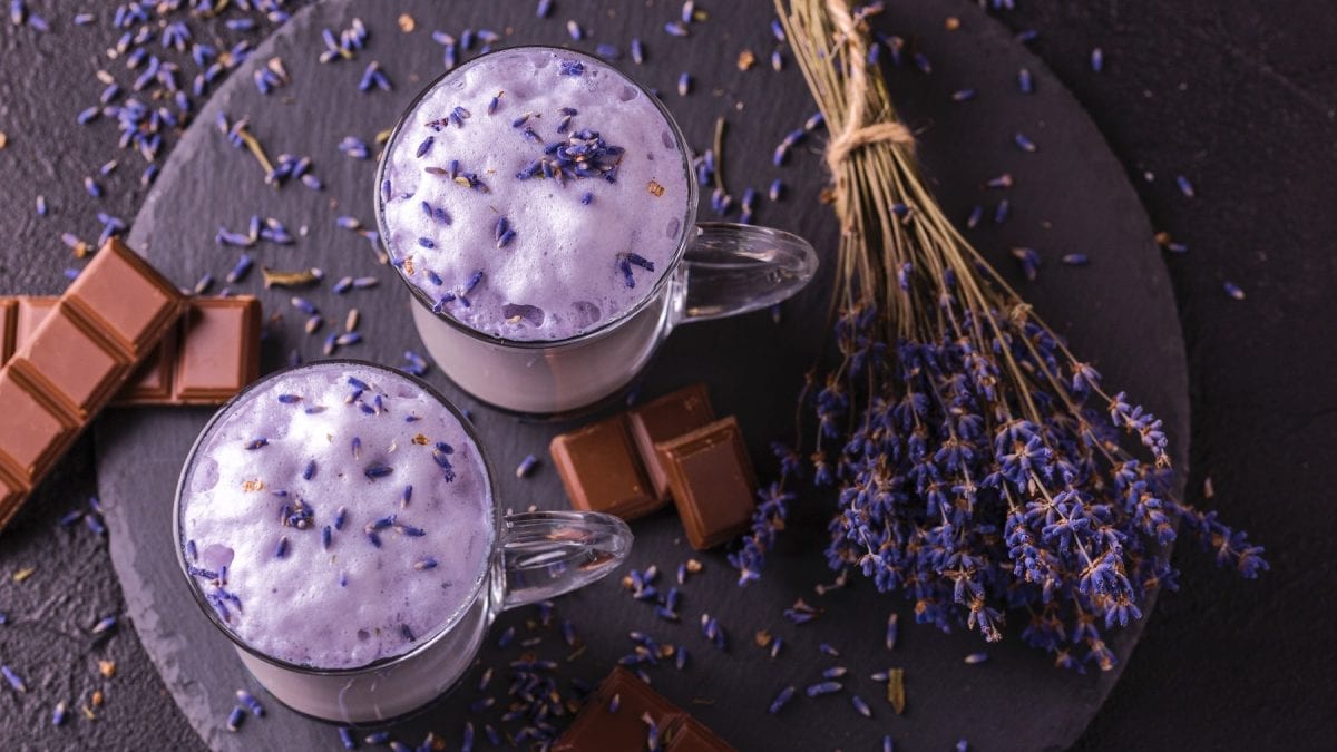 Cappuccino mit Lavendel und Schokolade in zwei Gläsern. daneben Schokoladenstücke und ein Lavendelbund.