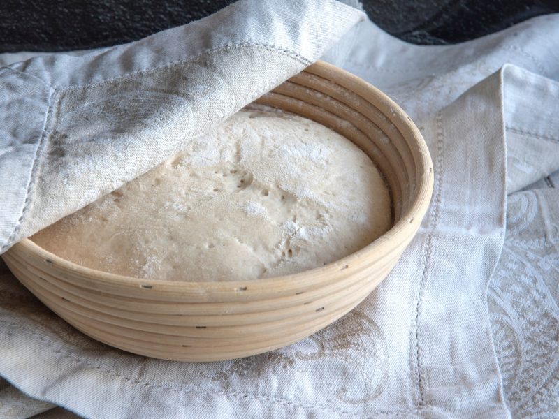 Draufsicht: Ein Korb auf einem Tuch. In dem Korb ist ein Hefeteig. Der ist von einem Teil des Tuches bedeckt.