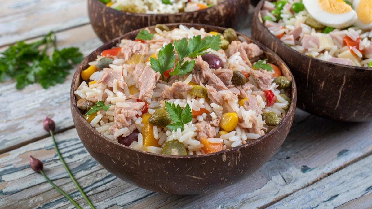 Draufsicht, schräg: Zwei Schalen Italienischer Reissalat mit Thunfisch. Die stehen auf einer Holzplatte. Drum herum liegt frische Petersilie.
