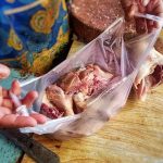 Draufsicht: Ein Mensch mit einer Schürze steht auf einem asiatischen Markt. In der Hand hält er eine offene Einkaufstüte. In der sind Karkassen vom Geflügel.
