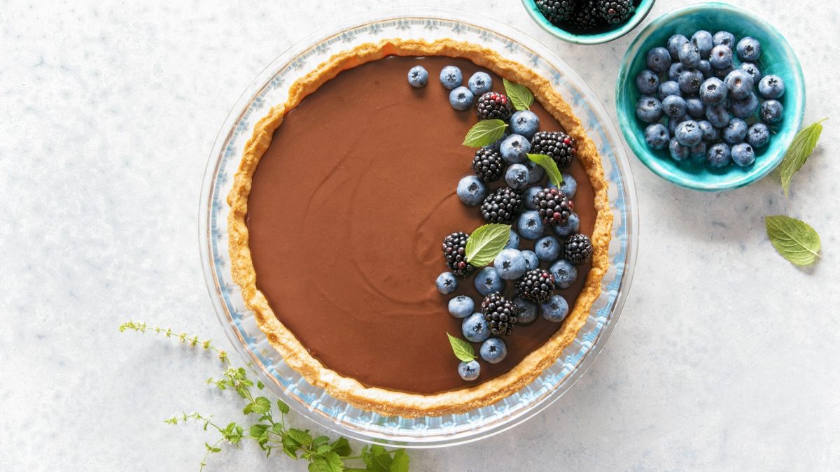 Draufblick: eine runde Schoko-Mousse-Tarte mit Beeren in einer Form. Daneben steht eine runde Schale mit Beeren.