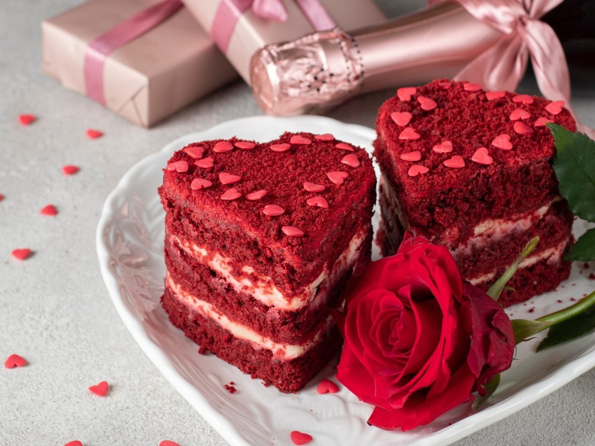 Draufsicht: zwei Kuchen auf einem hellen Teller. Im Hintergrund liege eine Flasche Sekt und zwei eingepackte Geschenke.