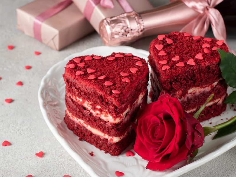 Draufsicht: zwei Kuchen auf einem hellen Teller. Im Hintergrund liege eine Flasche Sekt und zwei eingepackte Geschenke.