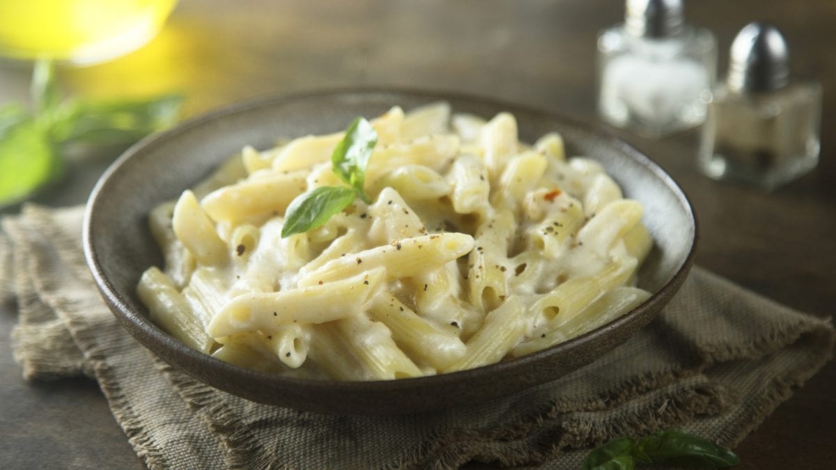 Ein dunkelbrauner Teller mit der Pasta auf einem dunklen Holztisch. Alles von schräg oben fotografiert.