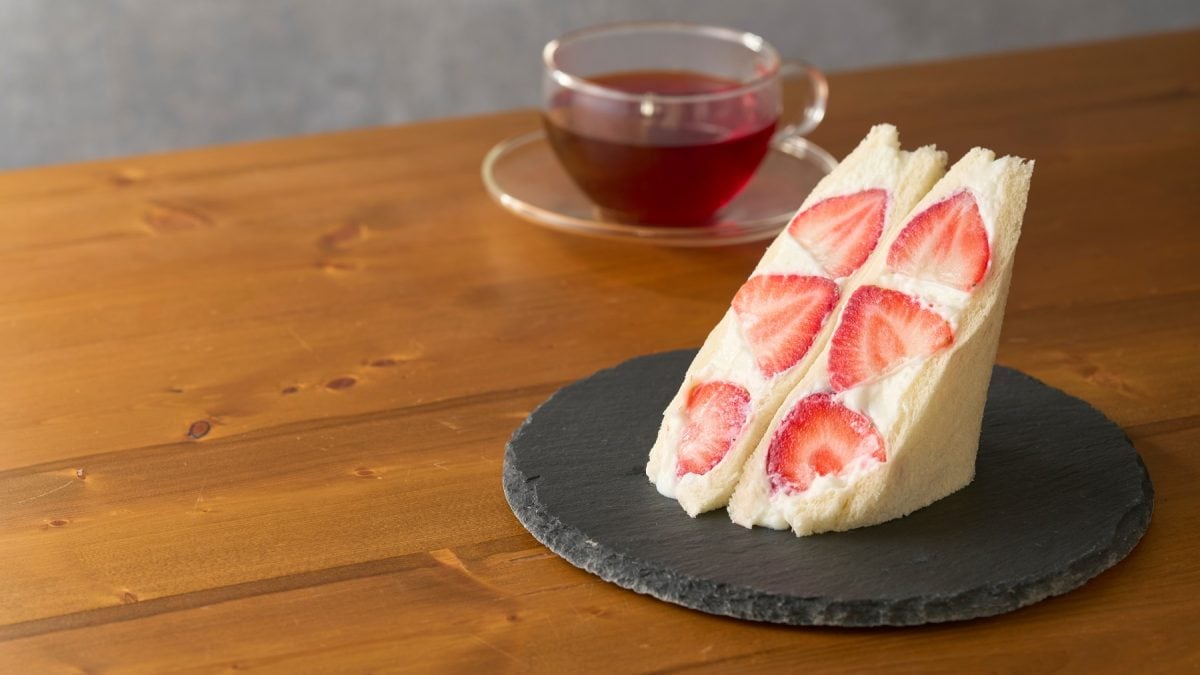 Aufgeschnittenes Fruit Sando mit Erdbeeren. Daneben eine Tasse Tee.