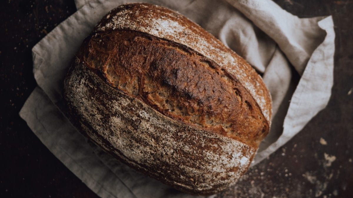 Glutenfreies Sauerteigbrot auf einem hellgrauen Geschirrtuch auf schwarzem Hintergrund.