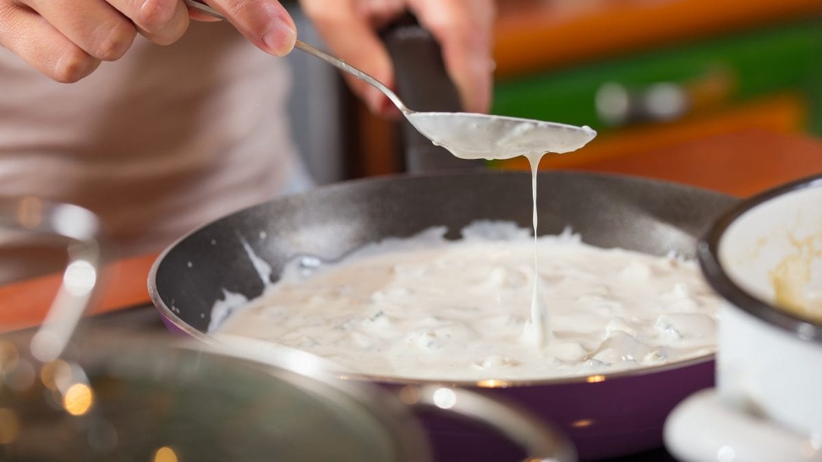 Frontalansicht: Eine Hand bereitet in einer Pfanne eine Gorgonzola-Sauce zu.