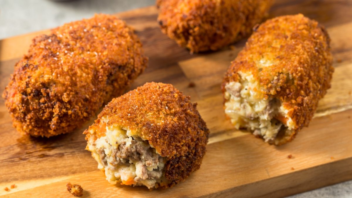 Einige Hackfleisch-Kroketten sehr nah fotografiert auf einem Holzbrett serviert.