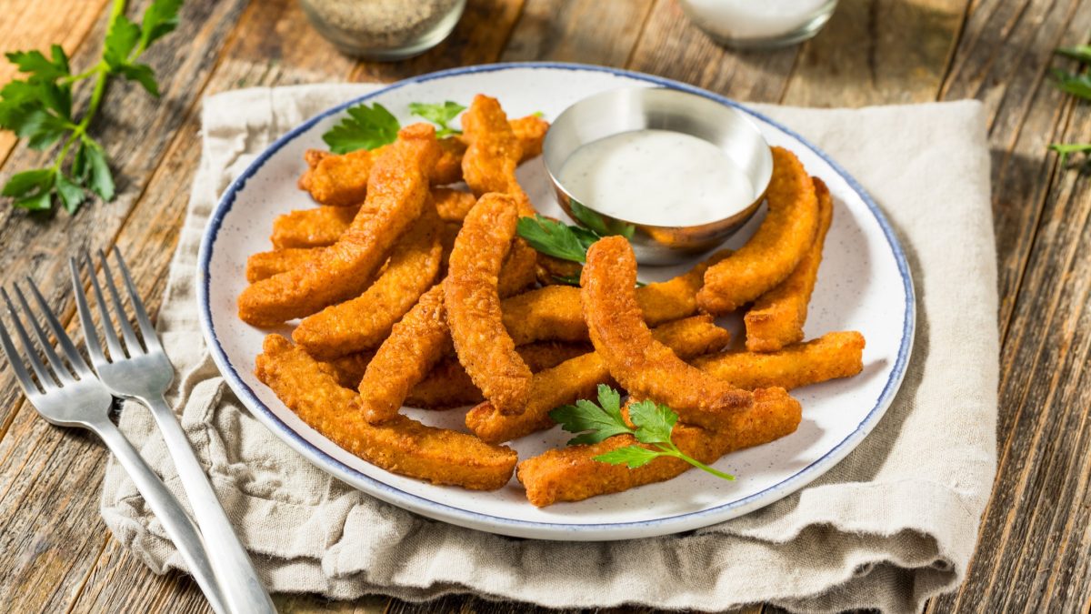 Mehrere Halloumi-Fries auf einem weißen Teller mit blauem Rand. Alles auf einem rustikalen Holztisch fotografiert.