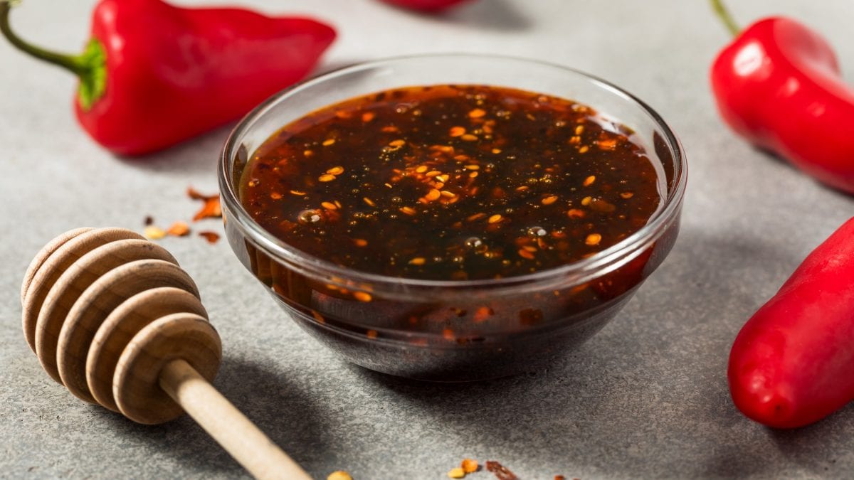 Eine kleine Glasschale mit dem Dip auf grauem Untergrund. Daneben Chilis und ein Holzhoniglöffel. Alles nah und von der Seite fotografiert.