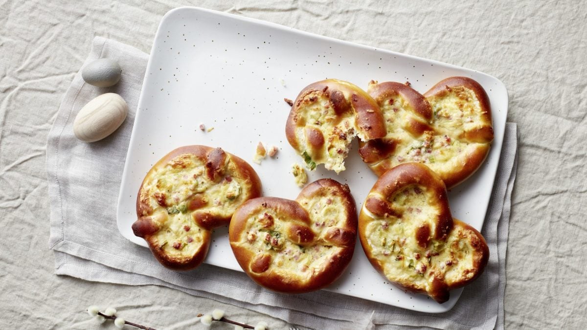 Überbackene Käsebrezeln Flammkuchenstyle auf einem weißen Teller mit hellem Stoffuntergrund.