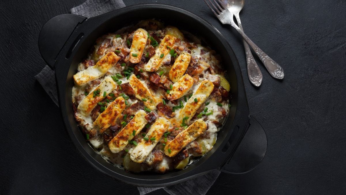 Eine schwarze Auflaufform mit dem Kartoffel-Rosenkohl-Gratin auf einem dunklen Untergrund.