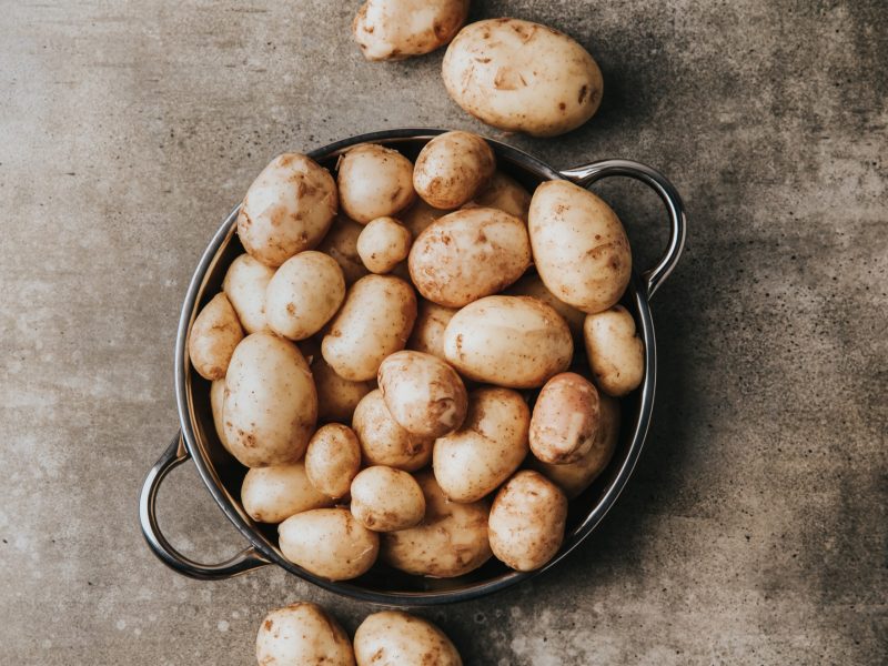 Ein silberner Topf mit Kartoffeln zum Kochen auf einer dunkelbraunen Fläche von oben fotografiert.
