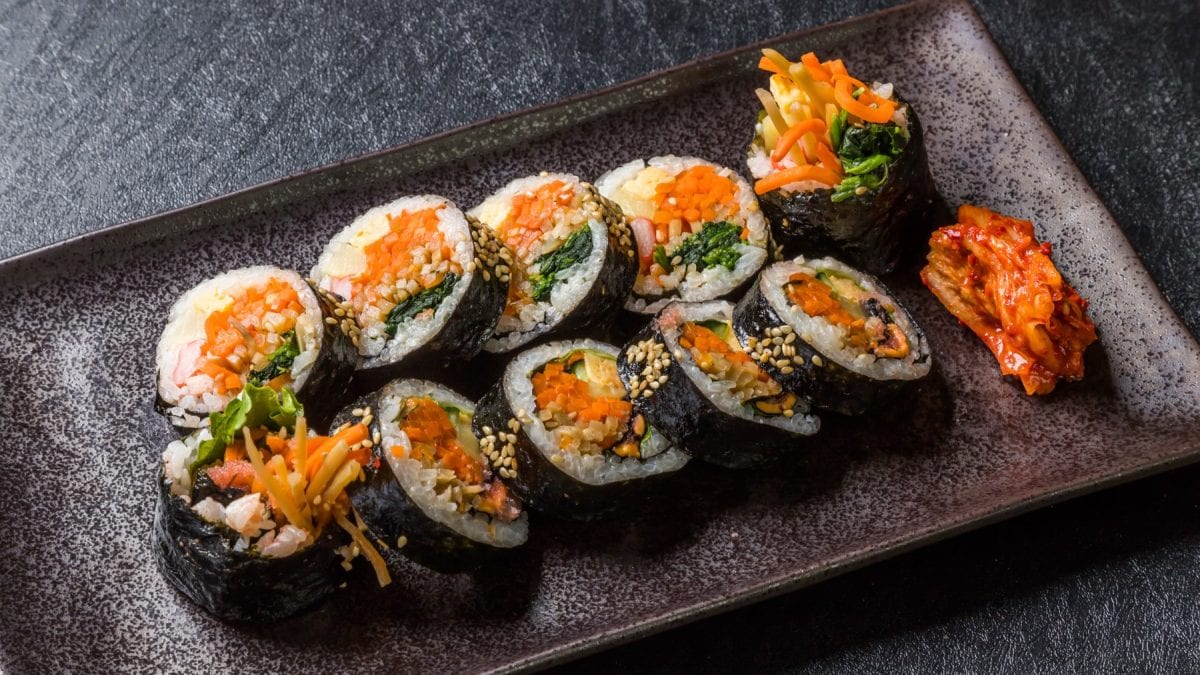 Kimbap auf einem schwarzen Teller serviert mit Kimchi. Der Hintergrund ist dunkelgrau.