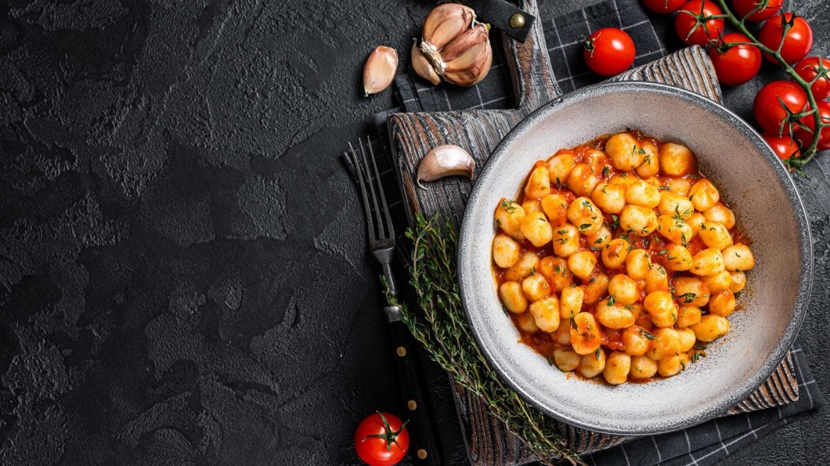 Draufsicht: Knoblauch-Gnocchi mit Tomatensauce auf schwarzem Untergrund.