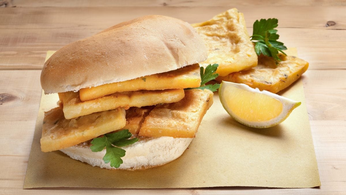Panelle siciliane in einem aufgeschnittenen Brötchen. Daneben ein Zitronenschnitz.