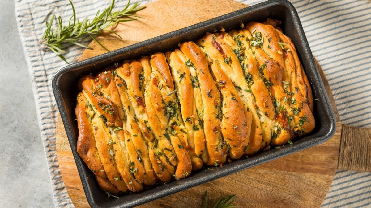 Eine Kastenform mit dem Pull-Apart-Bread auf einem Holzschneidebrett und grauem Tisch.