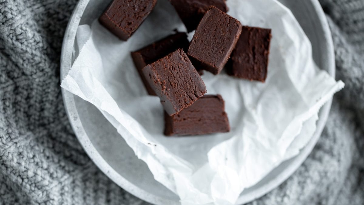 Rohkost-Brownies auf weißem Backpapier auf einem weißen Teller. Der Hintergrund ist grau.