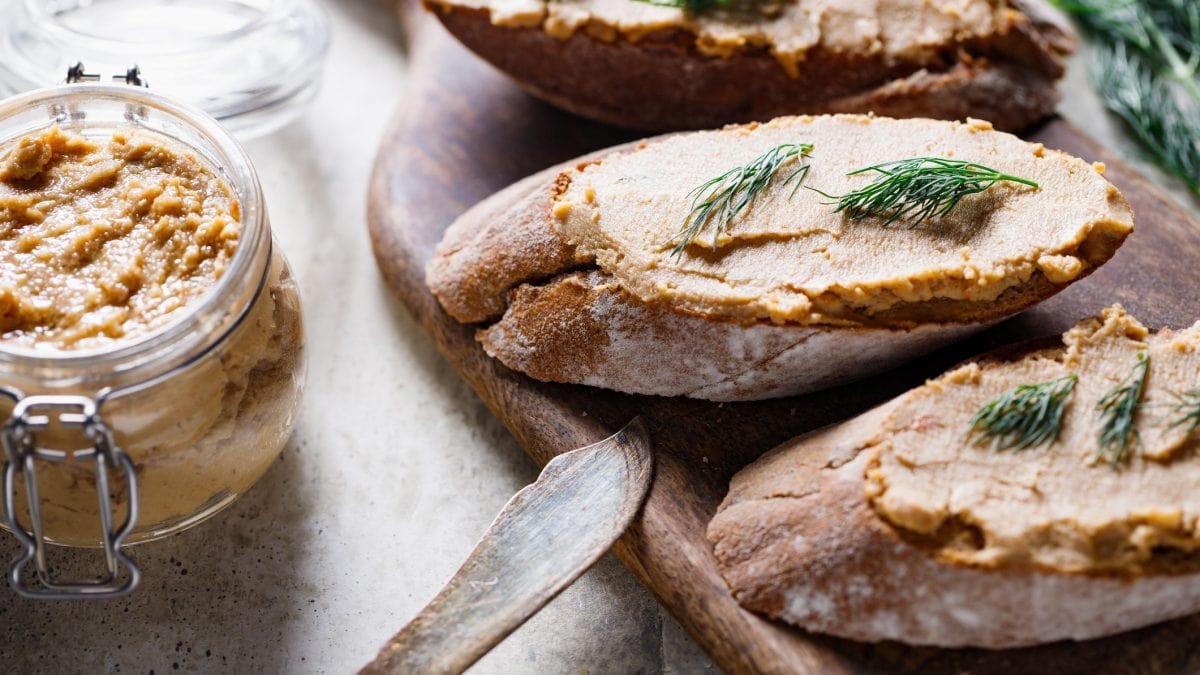 Draufblick, schräg: mehrere Scheiben Weißbrot, die mit einer Thunfischcreme mit Dill bestrichen sind. Daneben ist ein Glas mit der Creme sowie ein Messer.
