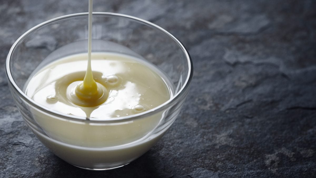 Vegane gezuckerte Kondensmilch wird von oben in eine Glasschale gegossen.