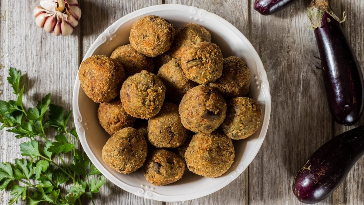 Draufsicht auf polpette di melanzane in einer weißen Schüssel. Drumherum Auberginen, Petersilie und Knoblauch.