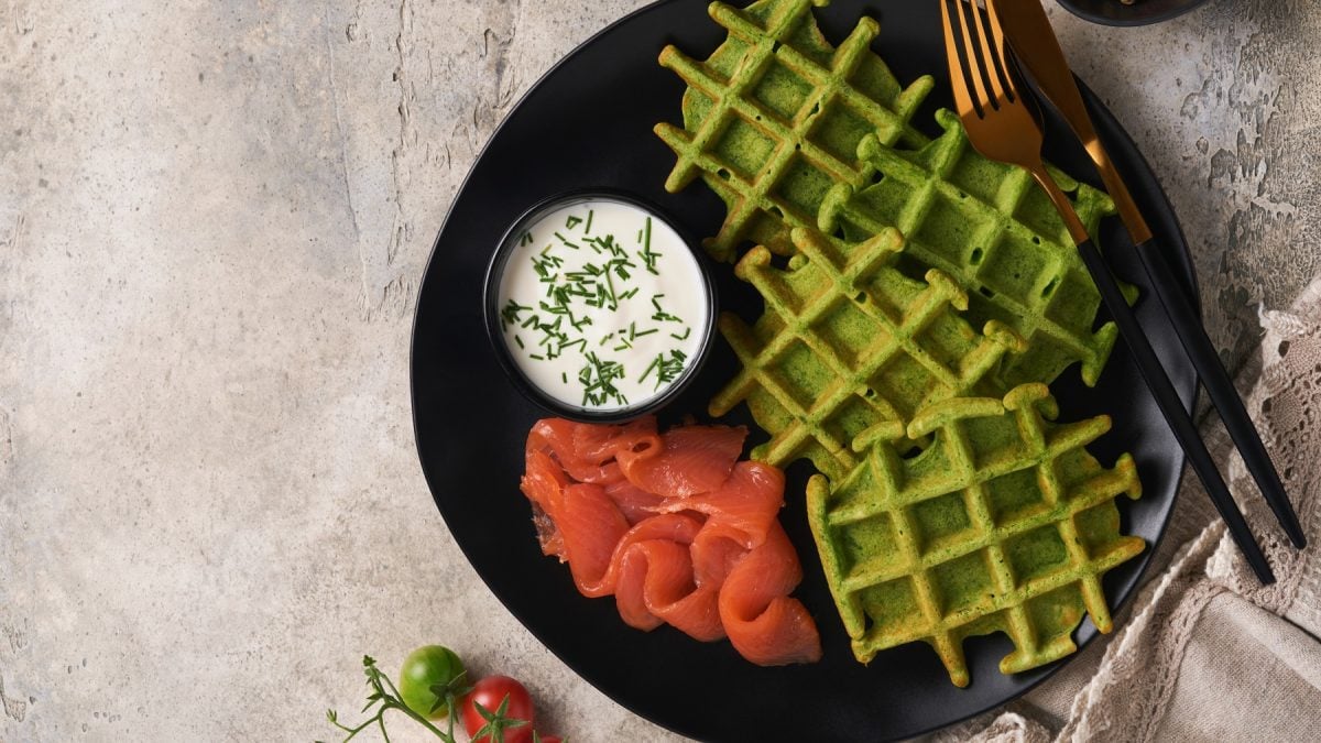 Ein schwarzer Teller mit den Bärlauchwaffeln und Räucherlachs auf grauem Steintisch. Alles direkt von oben fotografiert.