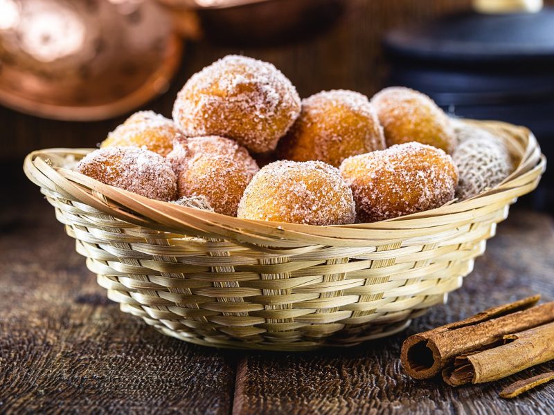 Bolinhos de chuva in einem Rattankorb. Daneben Zimtstangen