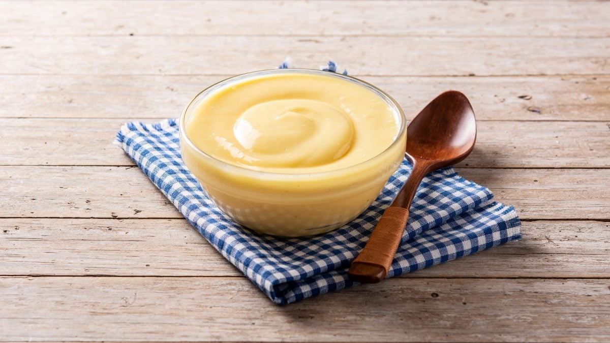 Crema pasticcera in einer Glasschüssel auf einem Geschirrtuch. Daneben ein Holzlöffel.
