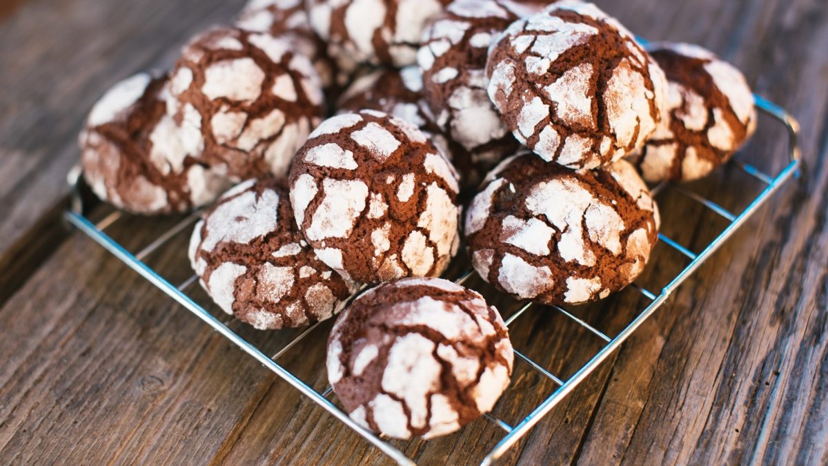 Draufsicht, schräg: Auf einem rustikalem Untergrund aus Holz liegt ein quadratisches Gitter auf dem Chocolate Crincle Cookies liegen.
