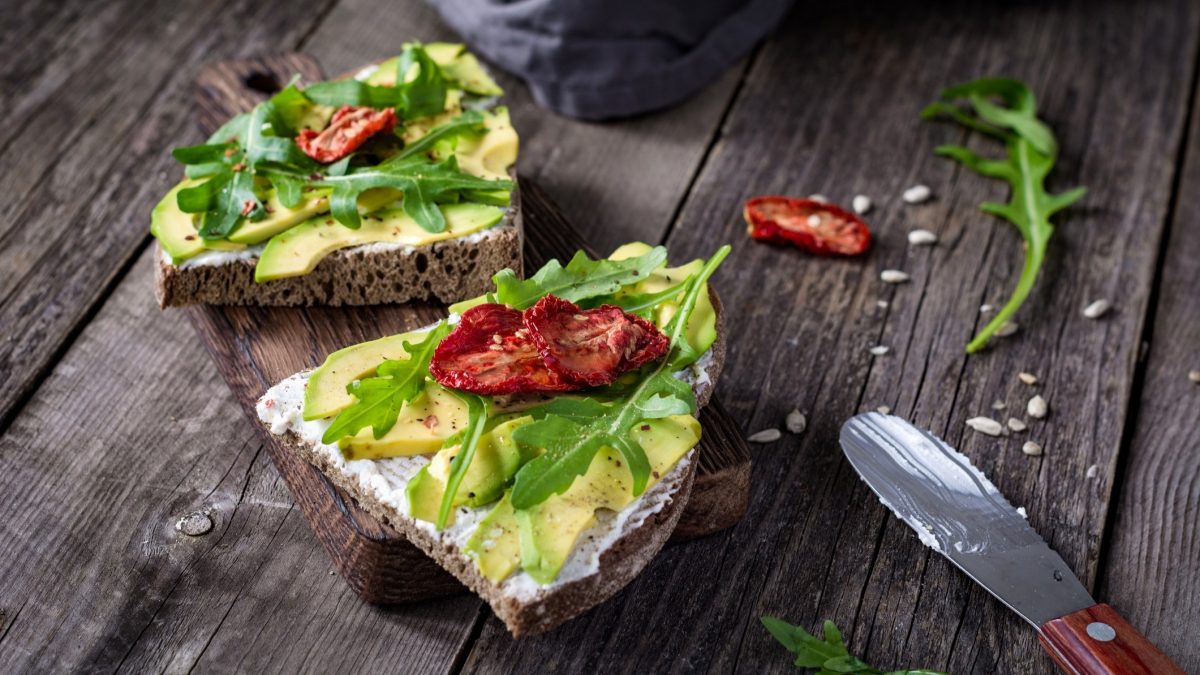 Draufsicht: Zwei Fancy-Avocado-Stullen liegen auf einem Holzbrettchen.