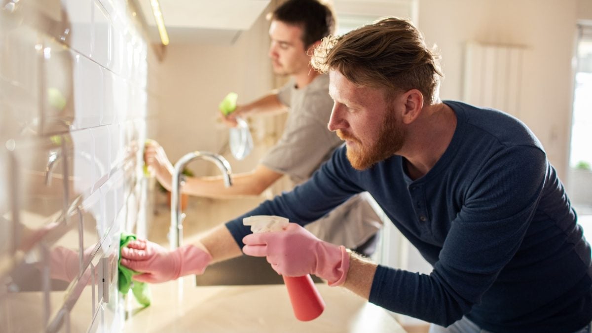 Frontal: Zwei Männer putzen eine Küche.
