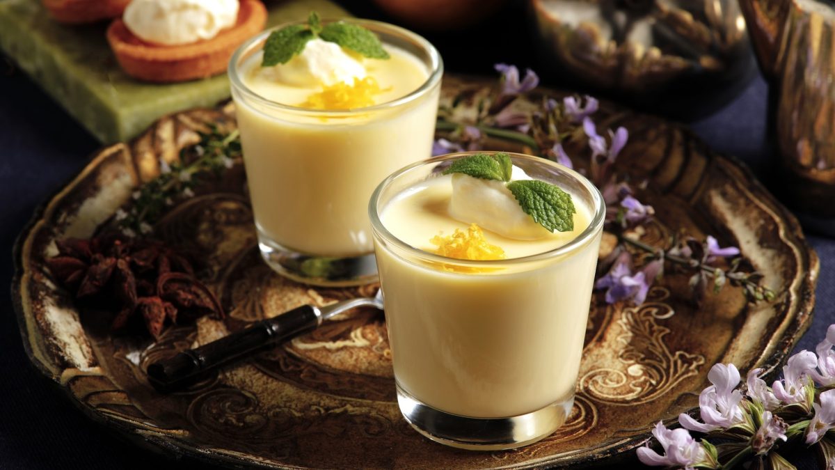Draufsicht: Zwei Gläser Lemon Posset auf einem Tablett. Das britische Dessert ist mit Sahne und Minze garniert.