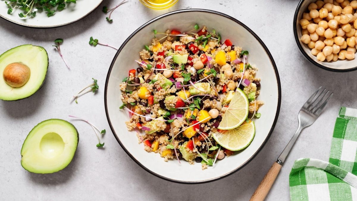 Draufblick: Auf einem hellen Untergrund steht eine runde Schüssel in der ein Quinoa-Salat mit Mango, Avocado, Bohnen ist.