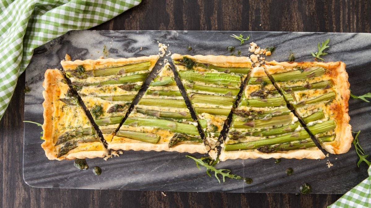 Draufsicht: eine Spargel-Quiche mit Bärlauch-Käse auf einem dunklen Untergrund.