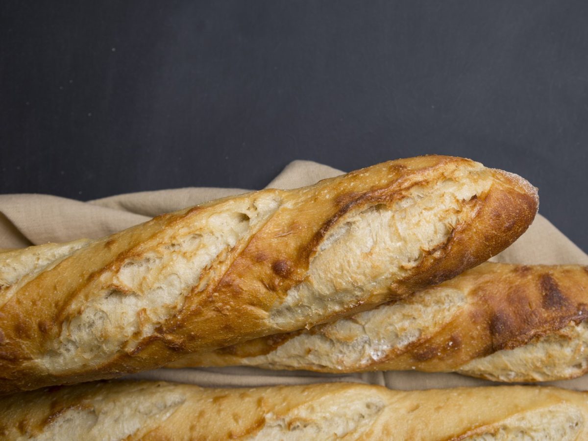 Ein angeschnittenes Baguette auf einem Holzbrett und grauem Hintergrund.