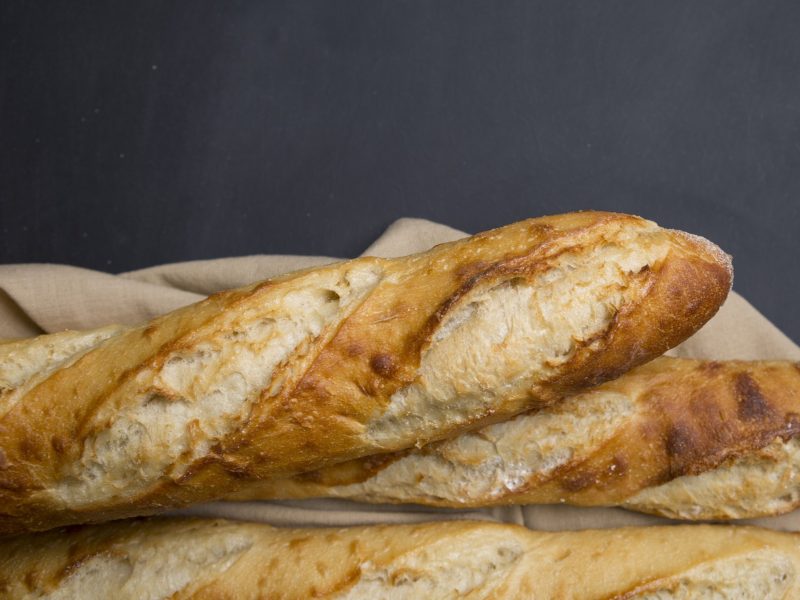 Ein angeschnittenes Baguette auf einem Holzbrett und grauem Hintergrund.